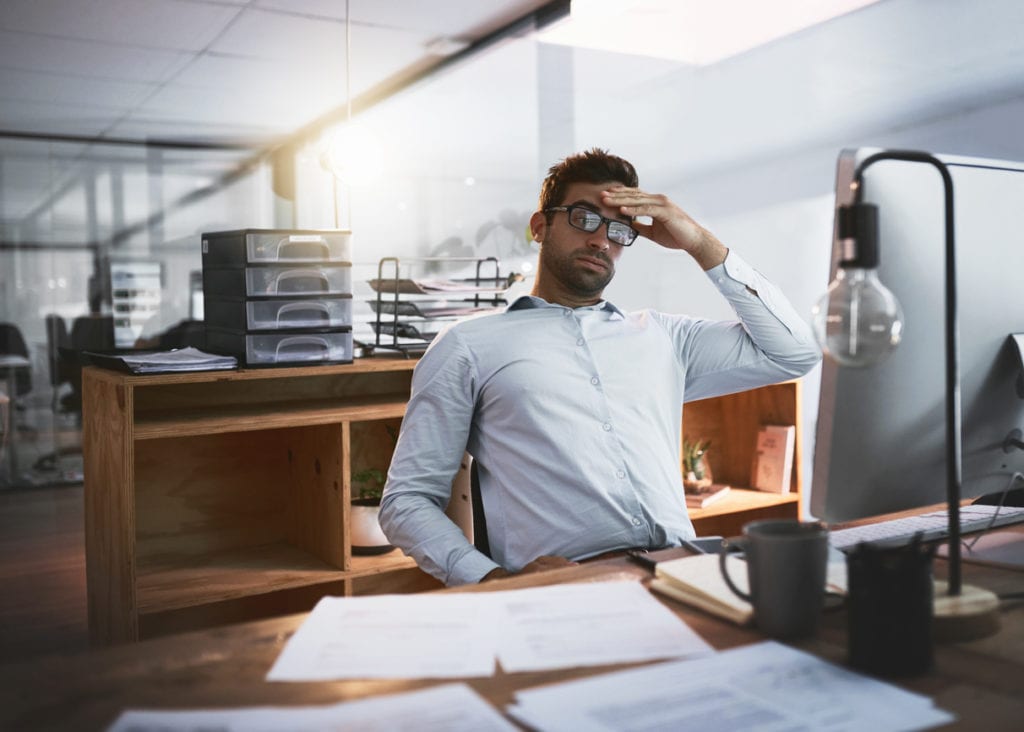 Shot of a young businessman looking stressed out while working late on a computer in an office