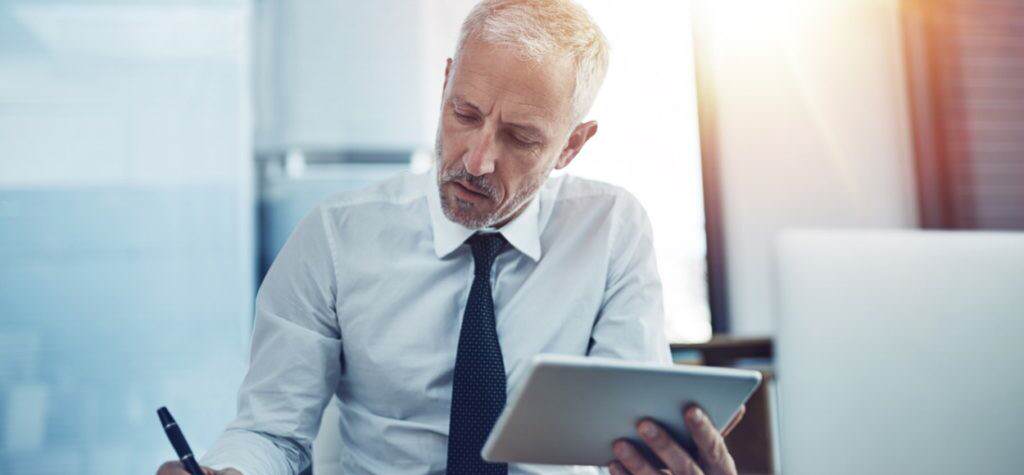 Old business man in smart suit working on tablet and writing something down