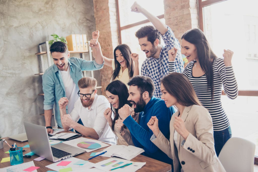 Success and team work concept. Group of business partners with raised up hands in light modern workstation, celebrating the breakthrough in their company