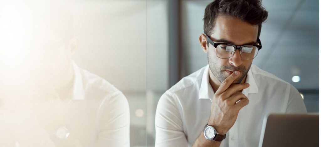 Man next to glass window looking at his laptop and thinking