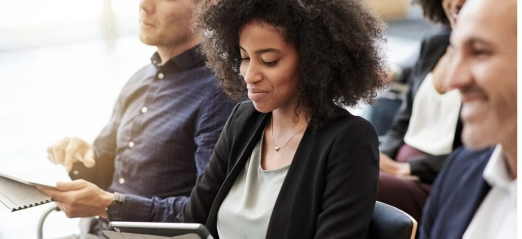 Focused shot on smartly dressed female sat in a conference looking down at a tablet