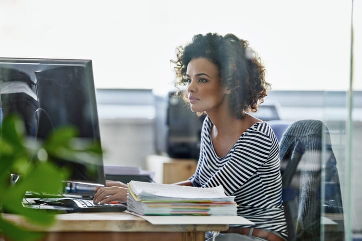 Dark skinned women wearing a black and white stripy top whilst working on a computer 