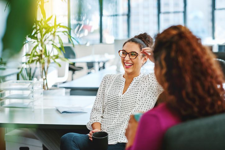 Two women laughing at a catch up in the office