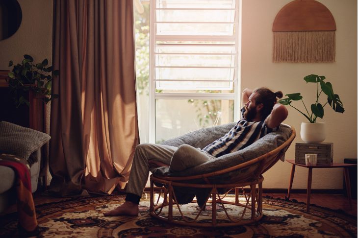 Man with bun in his hair relaxing on a comfy chair in his living room.