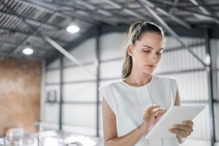 Female worker using digital tablet at brewery. Confident professional is in smart casuals. She is working at brightly lit beer industry.