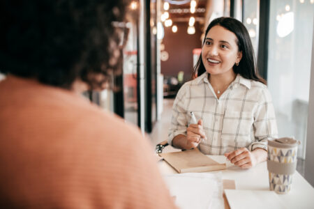 Two women havjng a meeting in a office whilst writing notes