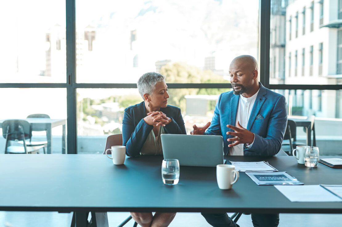 Two employees looking at something on a laptop whilst having a discussion