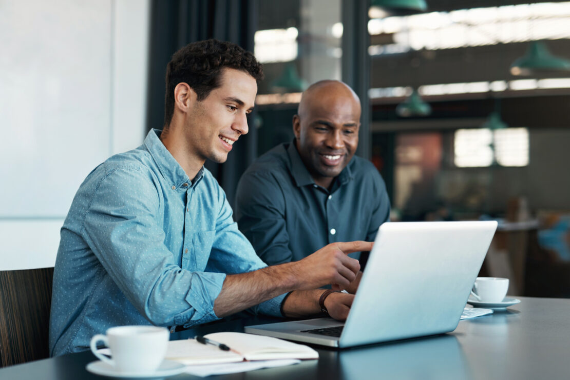 Two males looking at a laptop with mugs next to them