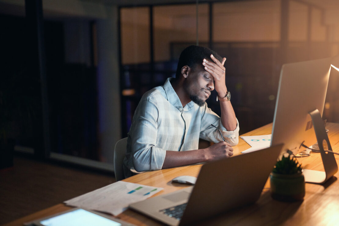 Stressed employee with headache looking at a computer screen