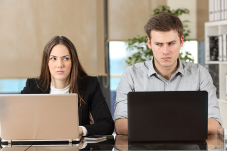 Two employees working next to each other giving angry faces.