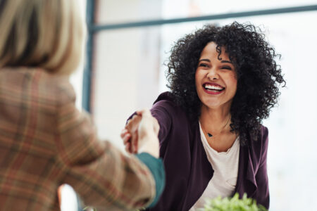 Two females shaking hands over a meeting table