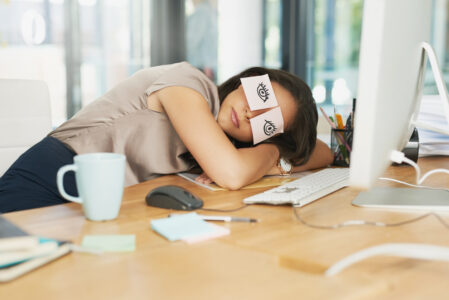 Women asleep on desk with paper over eyes