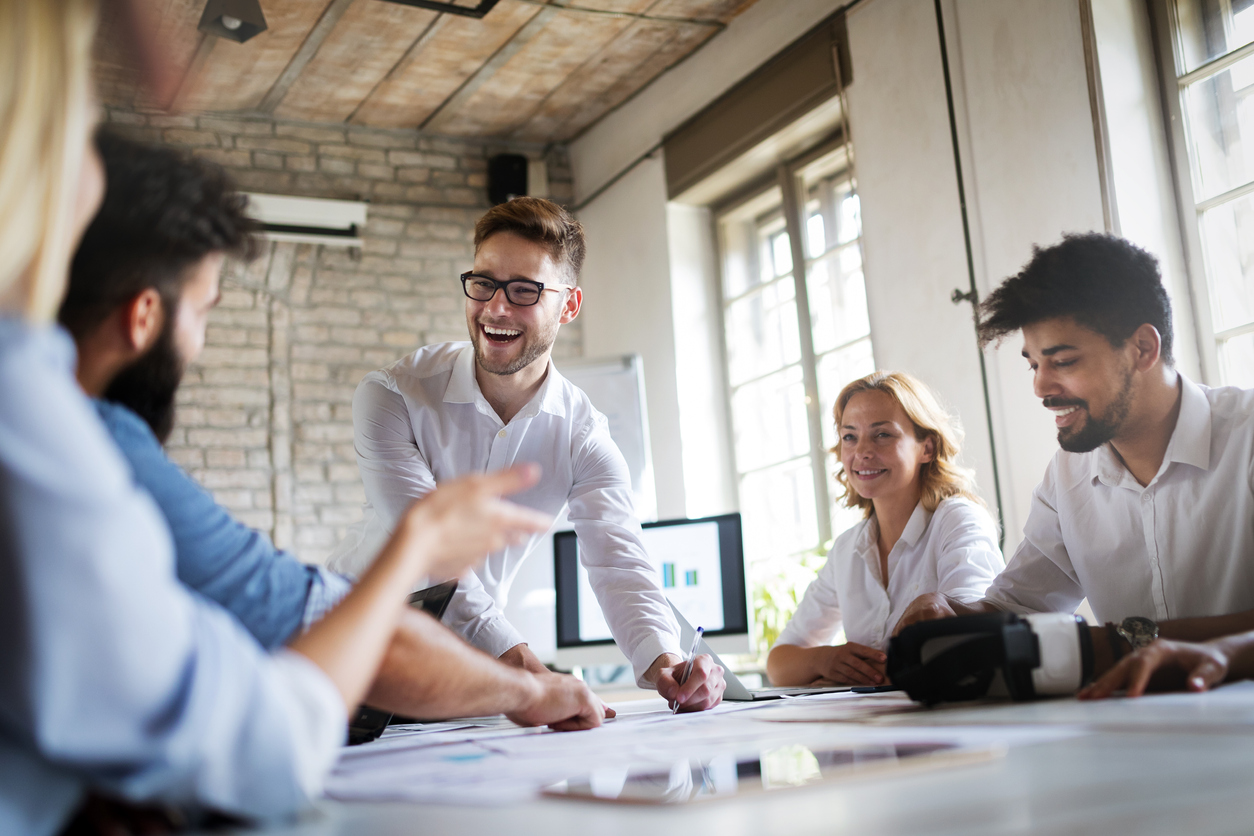 Male employees stood at the head of a meeting table smiling at his fellow employees