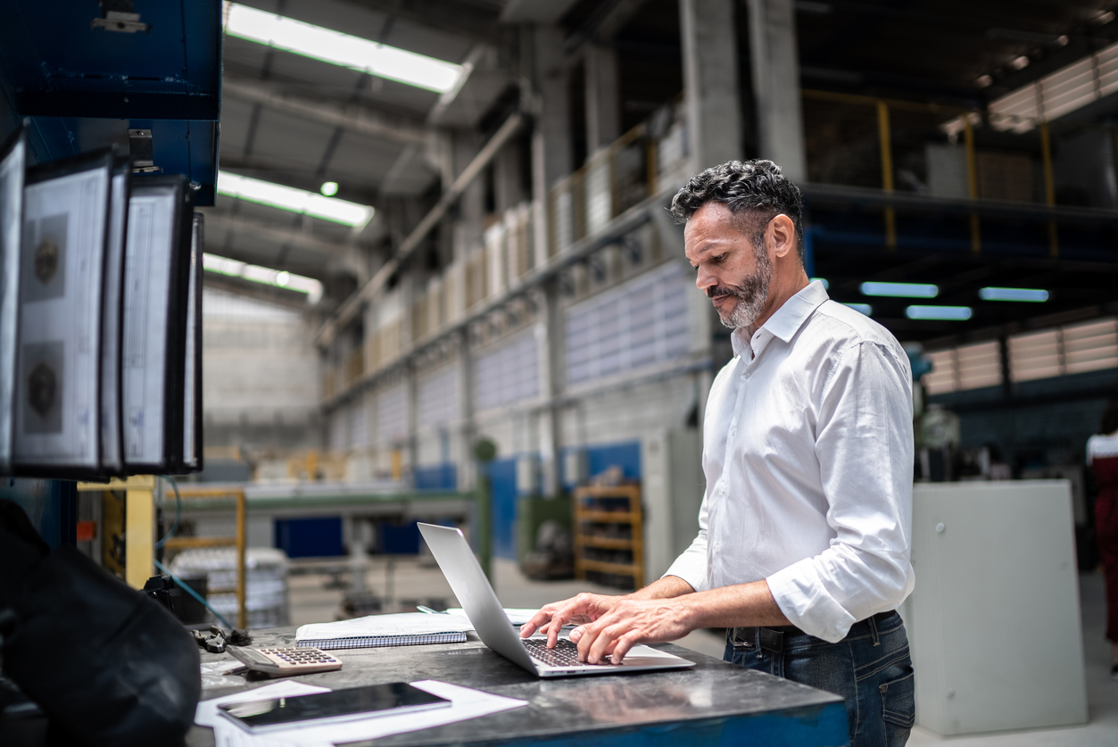 Smart man stood up at desk typing on his laptop