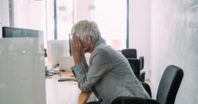 Male sat at desk with hands on his head hiding his face