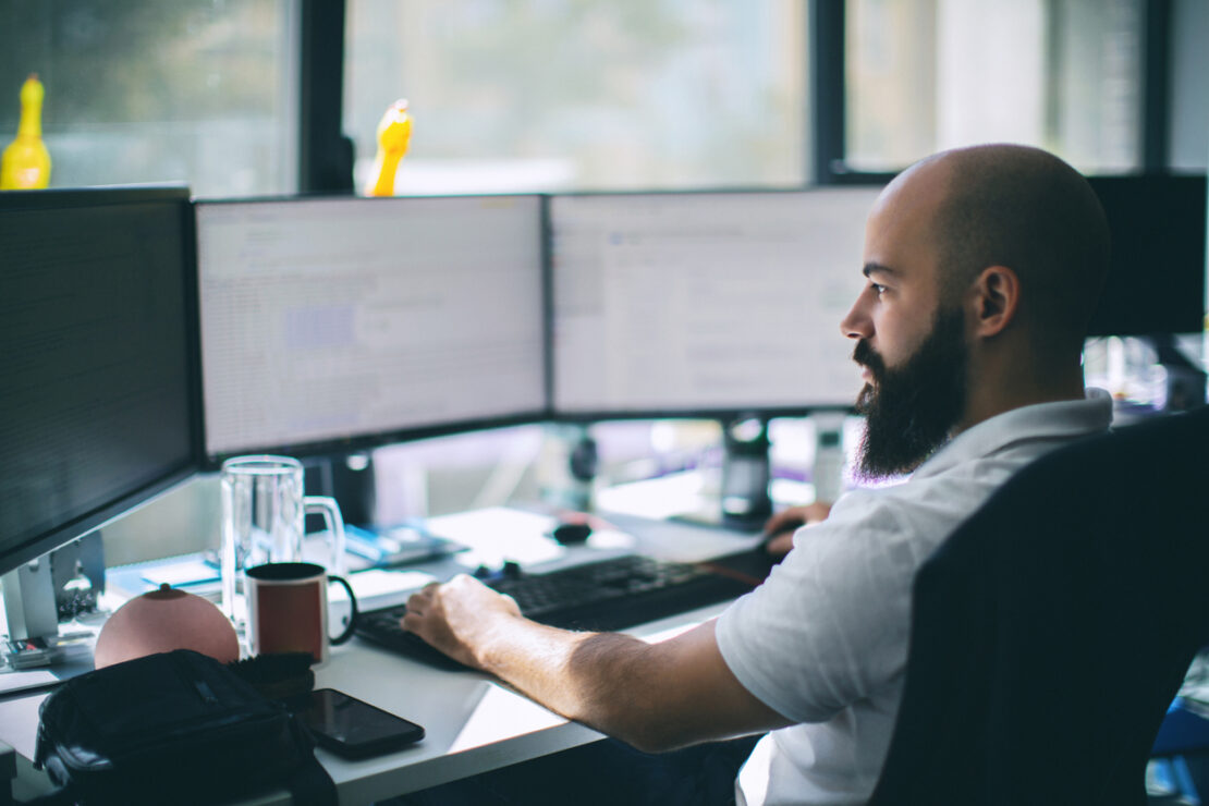 Male software employee looking at work over three screens