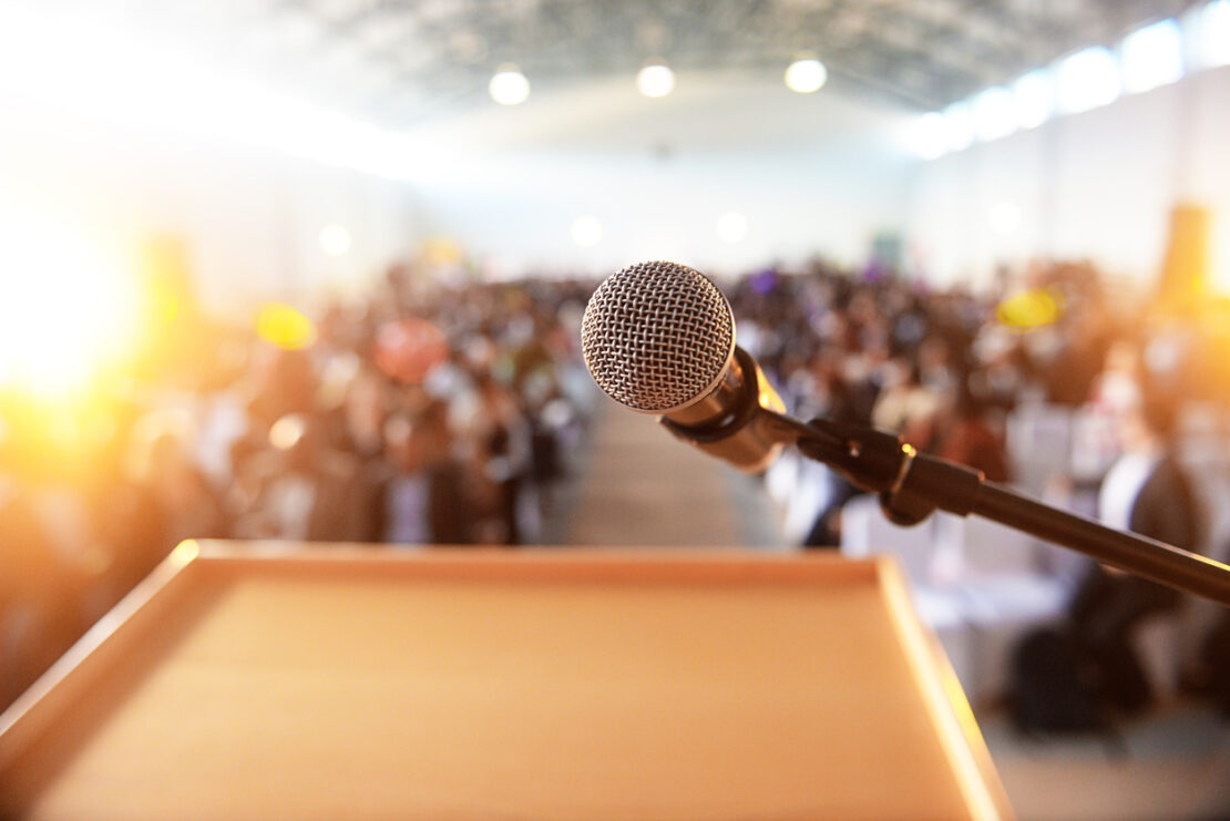 Focused image of a mic in front of a large room of people