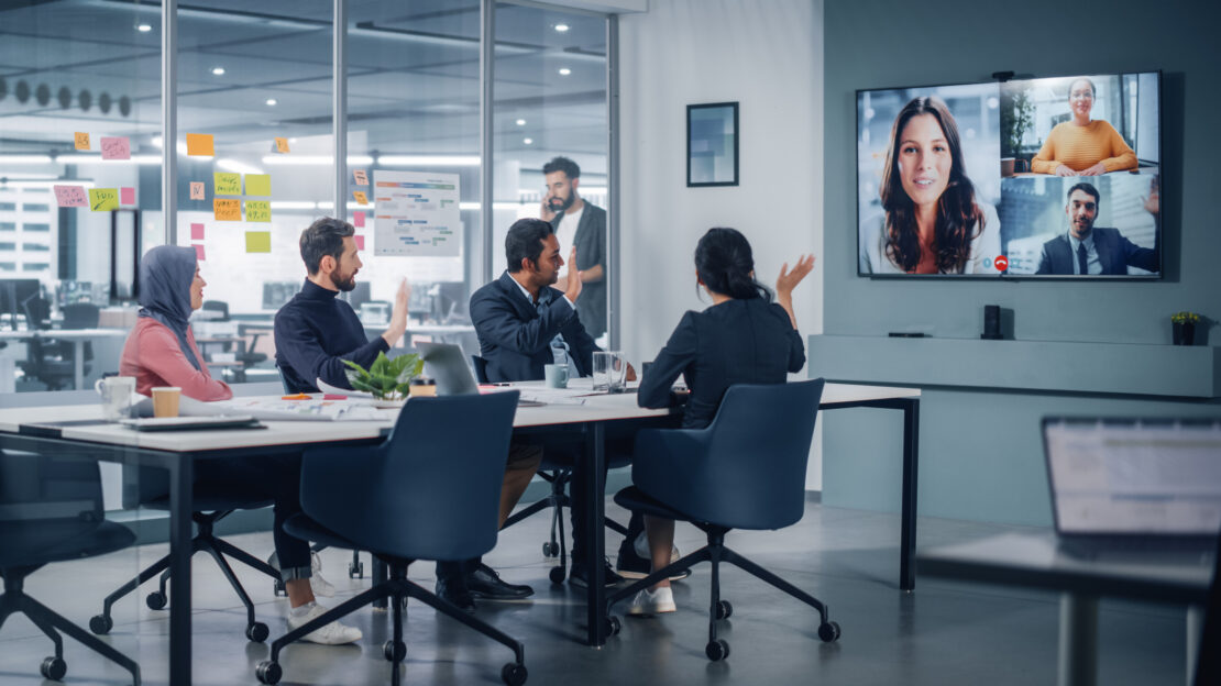 Four employees sat in meeting room talking to more employees on a video call