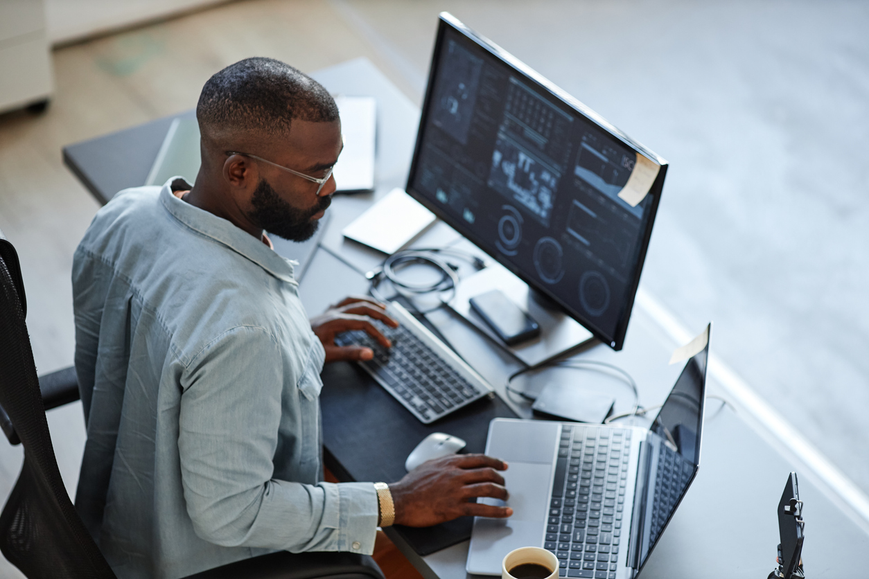 Dark skinned male working on a laptop and computer screen