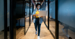 Female walking down office hallway on her laptop smiling