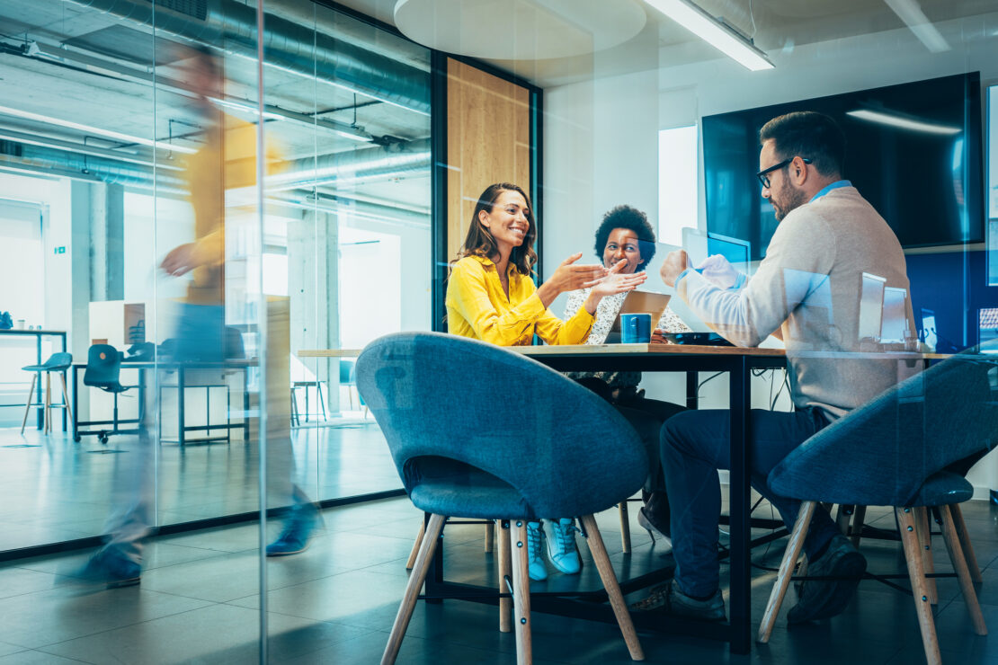 three employees sitting at a meeting table in glass windowed room