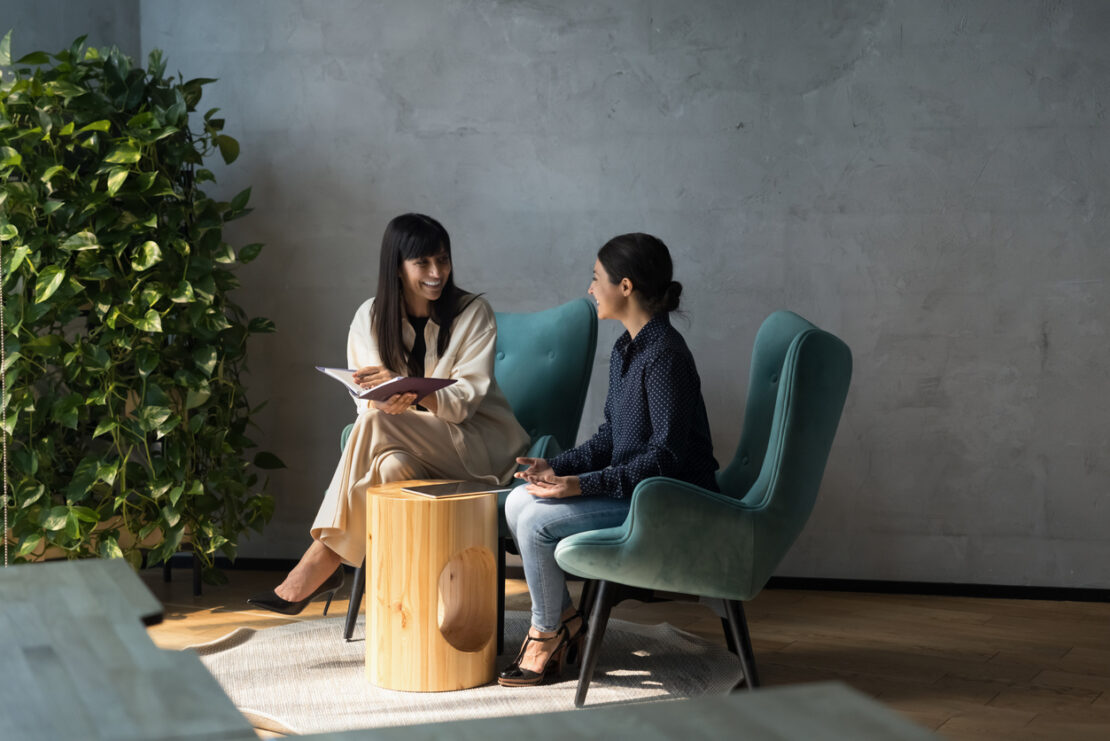 Two females sat on comfy chairs discussing with each other