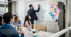 Male in professional suit writing notes on a whiteboard in a company meeting