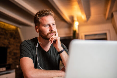 Overwhelmed young man listening to podcasts at home on laptop. Worried,trying to start a new business.