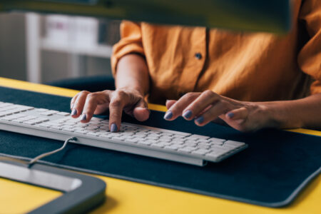 Close-up of a woman's hands typing on a white computer keyboard with a yellow desk, capturing a moment of business productivity.